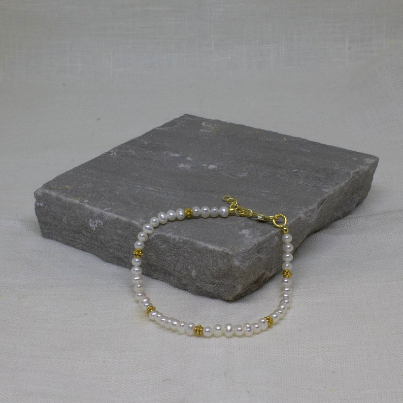 May include: A delicate pearl bracelet with gold accents. The bracelet is made of small white pearls and gold beads, and it has a simple clasp.