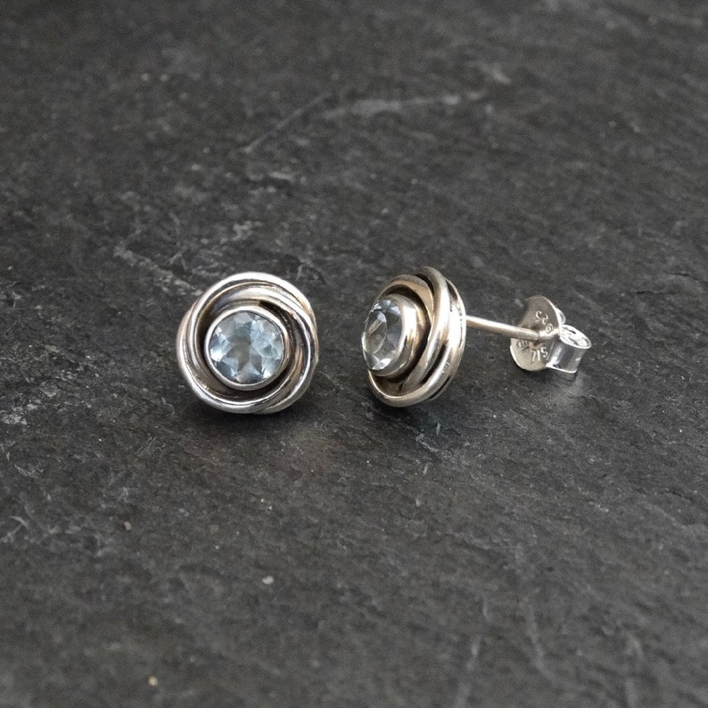 May include: A pair of silver earrings with a light blue gemstone set in a swirling design.