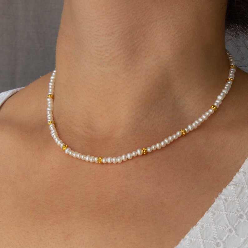 May include: A delicate pearl necklace with small gold beads interspersed throughout. The necklace is worn by a person, but the focus is on the jewelry itself.