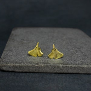 May include: A pair of gold-toned earrings shaped like ginkgo leaves. The earrings are small and delicate, and they would make a great gift for someone who loves nature.