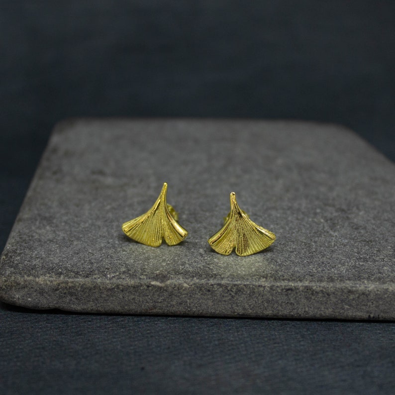 May include: A pair of gold-toned earrings shaped like ginkgo leaves. The earrings are small and delicate, and they would make a great gift for someone who loves nature.