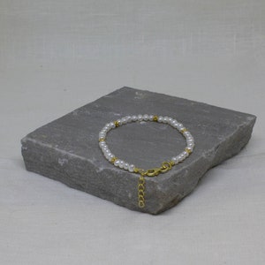 May include: A delicate pearl bracelet with gold accents. The bracelet is made of small white pearls and gold beads, and it has a gold clasp.
