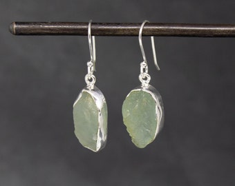 Può includere: Un paio di orecchini d'argento con pietre di acquamarina verde chiaro. Le pietre sono grezze e hanno una forma naturale irregolare.