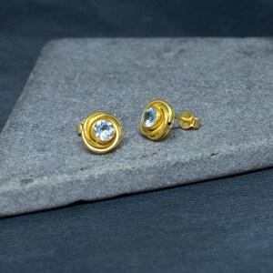 May include: A pair of gold-toned earrings with a light blue gemstone in the center of each earring.