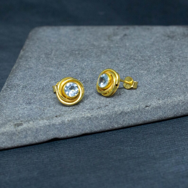 May include: A pair of gold-toned earrings with a light blue gemstone in the center of each earring.