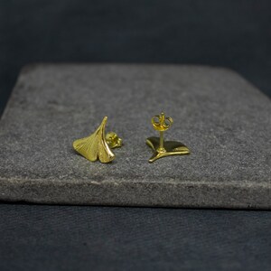 May include: A pair of gold-toned ginkgo leaf earrings. The earrings are small and delicate, and they have a simple, elegant design.