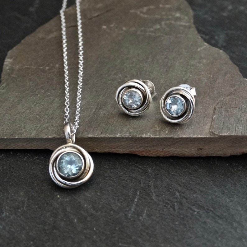 May include: A silver necklace and earrings set with a light blue gemstone in a swirl design.