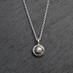 May include: A silver chain necklace with a silver pendant featuring a white pearl in a circular design.