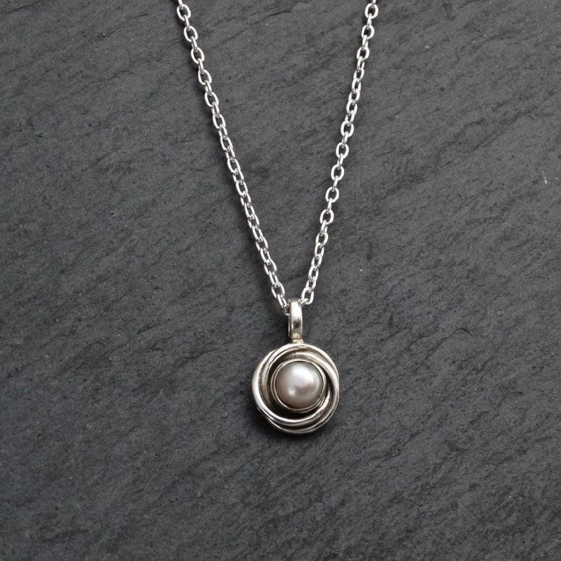 May include: A silver chain necklace with a silver pendant featuring a white pearl in a circular design.