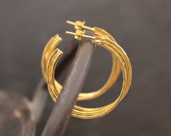 May include: Gold hoop earrings with a layered design. The earrings are made of multiple thin hoops that are stacked on top of each other.