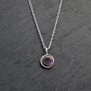 K&ouml;nnte beinhalten: Eine silberne Kettenkette mit einem Anh&auml;nger, der einen violetten Amethyst-Edelstein in einem silbernen Wirbeldesign zeigt.