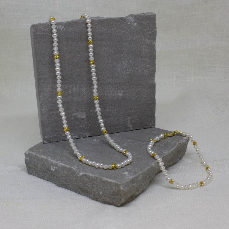 May include: A white pearl necklace and bracelet set with gold accents. The necklace is longer than the bracelet.
