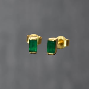 May include: A pair of gold earrings with emerald green rectangular stones.