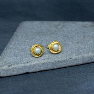 May include: A pair of gold stud earrings with a white pearl in the center of each earring.