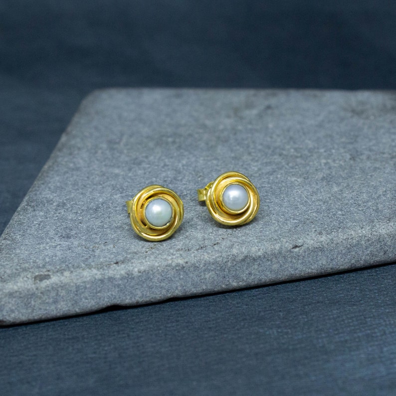 May include: A pair of gold stud earrings with a white pearl in the center of each earring.