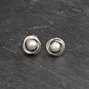 May include: A pair of silver earrings with a pearl in the center of each earring. The earrings are in the shape of a swirl.
