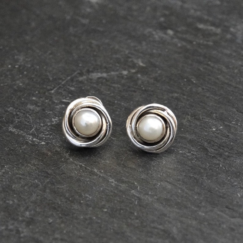 May include: A pair of silver earrings with a pearl in the center of each earring. The earrings are in the shape of a swirl.