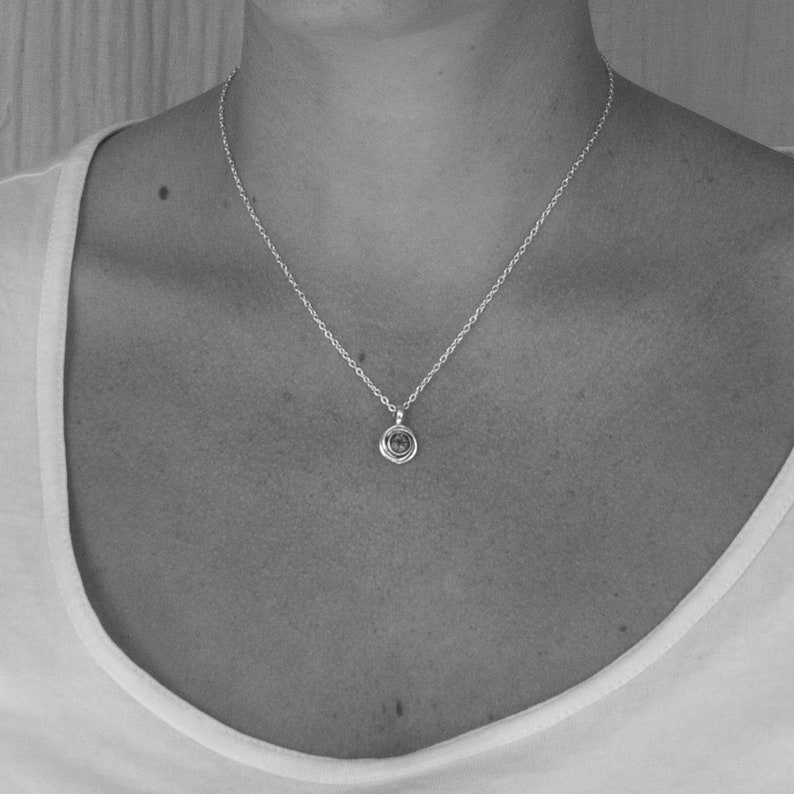 May include: A silver chain necklace with a small, round pendant. The pendant has a textured, circular design.