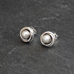 May include: A pair of silver stud earrings with a white pearl in the center of each earring. The earrings are in the shape of a rose.