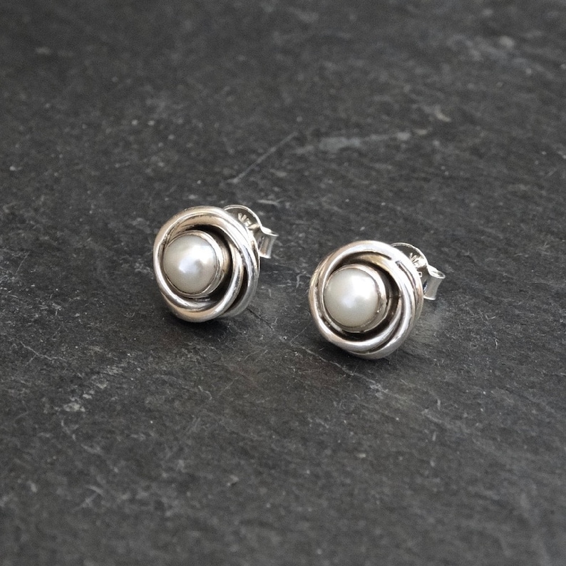 May include: A pair of silver stud earrings with a white pearl in the center of each earring. The earrings are in the shape of a rose.