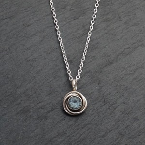 May include: A silver chain necklace with a pendant featuring a blue gemstone set in a silver swirl design.