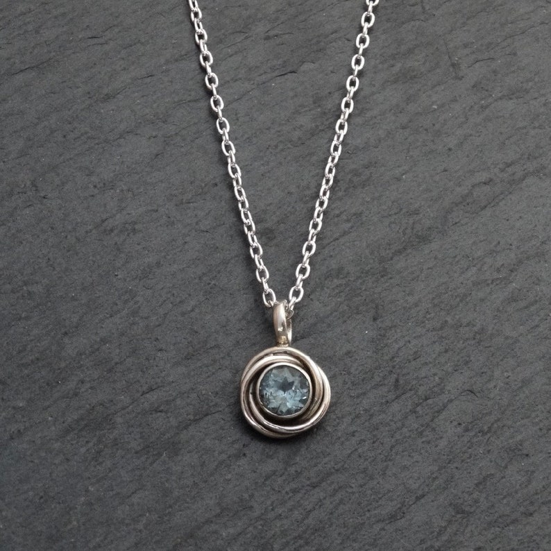 May include: A silver chain necklace with a pendant featuring a blue gemstone set in a silver swirl design.