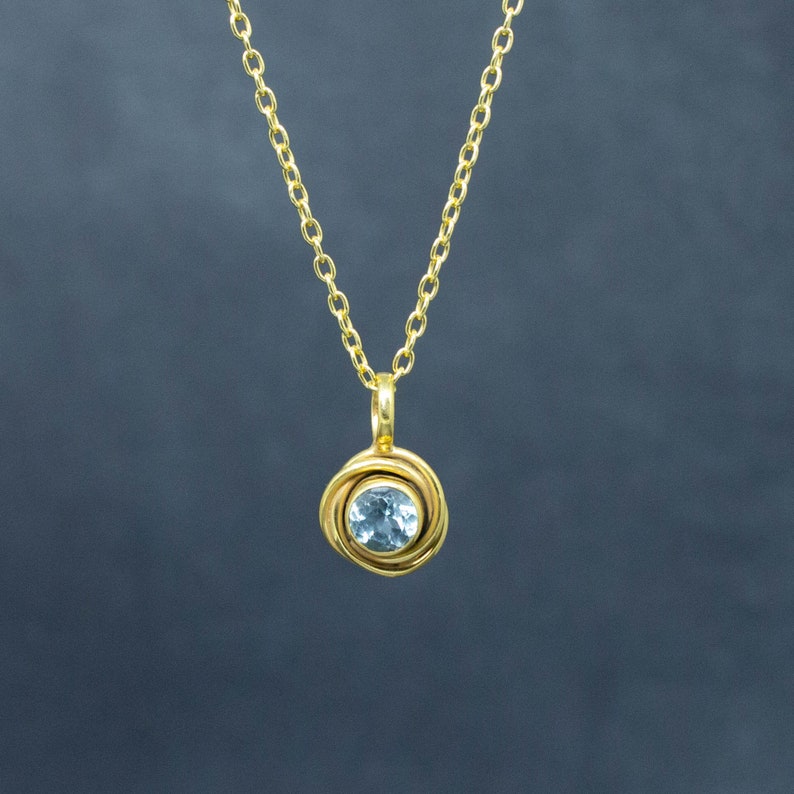 May include: A gold chain necklace with a pendant featuring a light blue gemstone set in a gold swirl design.