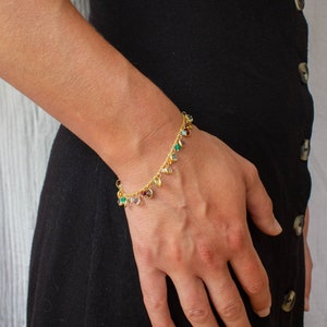 May include: A gold chain bracelet with colorful gemstone charms. The bracelet is on a person's wrist.