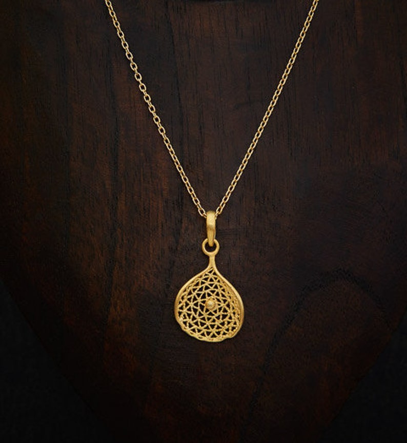 May include: A gold necklace with a delicate chain and a pendant shaped like a teardrop with a geometric design. The pendant has a small circle in the center.