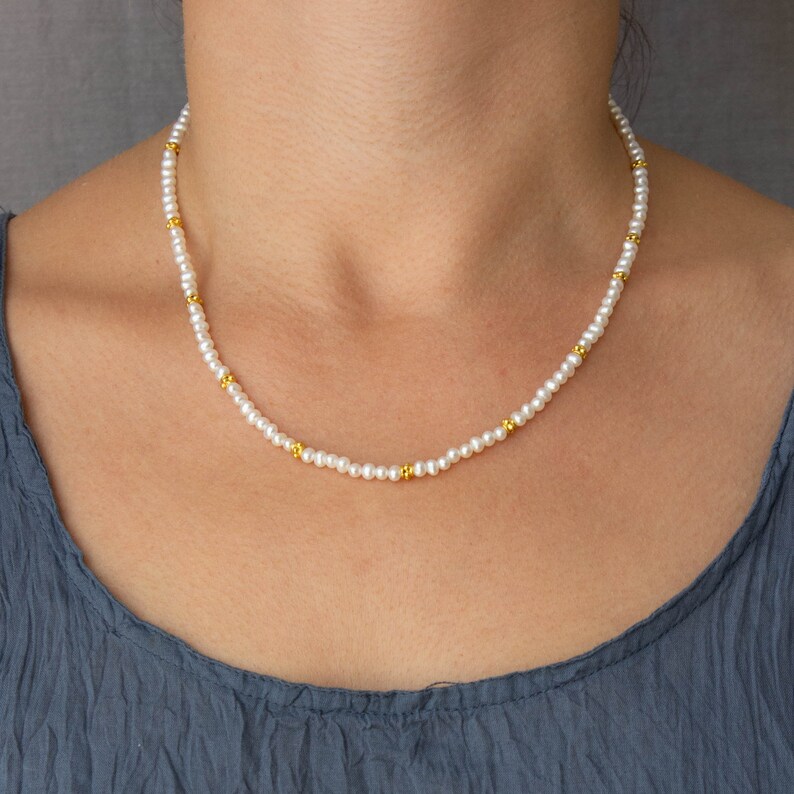 May include: A delicate white pearl necklace with small gold beads interspersed throughout. The necklace is worn by a person, but the focus is on the necklace itself.
