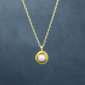 May include: A gold chain necklace with a pearl pendant. The pendant is a circle of gold wire with a pearl in the center.