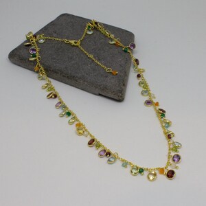 May include: A gold chain necklace with a variety of colorful gemstones, including amethyst, aquamarine, citrine, garnet, peridot, and topaz.