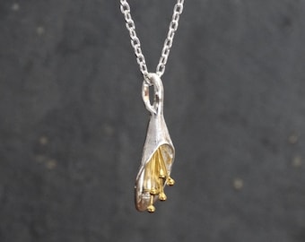 May include: A silver necklace with a pendant shaped like a flower. The flower is made of silver and has gold accents. The pendant is hanging from a silver chain.