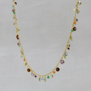 May include: A gold chain necklace with a variety of colorful gemstones, including amethyst, aquamarine, carnelian, emerald, garnet, and peridot.