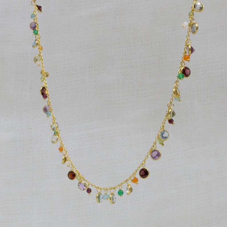 May include: A gold chain necklace with a variety of colorful gemstones, including amethyst, aquamarine, carnelian, emerald, garnet, and peridot.