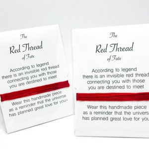 May include: Two red string bracelets wrapped around white display cards. Each card features the text: The Red Thread of Fate. According to legend there is an invisible red thread connecting you with those you are destined to meet. Wear this handmade piece as a reminder that the universe has planned great love for you.