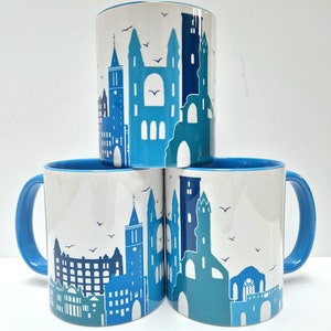 May include: Three blue and white ceramic mugs with a cityscape design. Each mug features a different silhouette of a city skyline with buildings and birds.