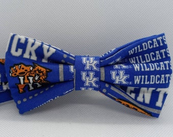 Może przedstawiać: Niebieski krawat muszka z białym i pomarańczowym logo Kentucky Wildcats i napisami "Wildcats" i "Kentucky".