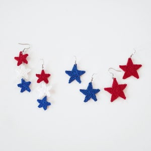 May include: Three pairs of crocheted star earrings in red, white, and blue. One pair features three stars, while the other two pairs each have one star.