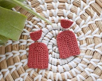 May include: A pair of terracotta-colored crocheted earrings with a small, round top and a larger, arched bottom.