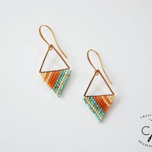 Op de afbeelding: Een paar gouden driehoekige oorbellen met een kralenontwerp. De kralen zijn in tinten turquoise, oranje en crème.