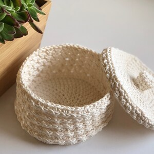 May include: A white crocheted storage basket with a lid. The basket is round and has a woven pattern. The lid has a small crocheted knob.