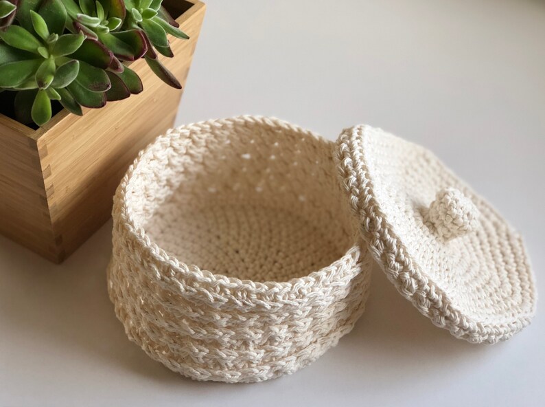 May include: A white crocheted storage basket with a lid. The basket is round and has a woven pattern. The lid has a small crocheted knob.