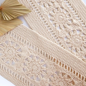 May include: Two cream-colored, rectangular crochet doilies with intricate openwork patterns. One doily is partially visible, and the other is in the foreground. A dried palm leaf fan is in the upper left corner, adding a natural element to the composition.