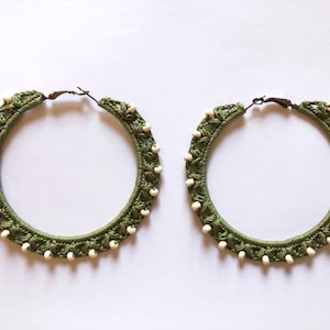 May include: A pair of large green hoop earrings with white beads around the edge.