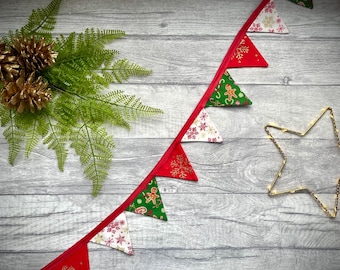 May include: A festive Christmas banner with red and green triangle flags, adorned with snowflakes and gingerbread men, strung on a red ribbon. Gold-painted pinecones and a star-shaped light add to the holiday decor.