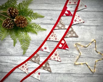 May include: A festive Christmas banner with red ribbon and triangle flags. The flags feature holiday patterns in red, white, and gray. Gold-painted pinecones and a star-shaped light add to the seasonal decor.