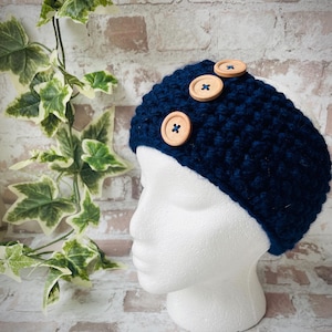 Puede incluir: Una diadema de crochet azul marino con tres botones de madera.