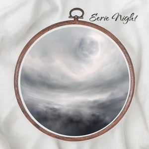 May include: A round wooden embroidery hoop with a white fabric background. The fabric has a dark gray and white cloudy sky image with a bright white moon in the center. The text "Eerie Night" is written in black cursive above the hoop.