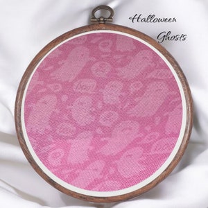 May include: A pink fabric embroidery hoop with a pattern of ghosts. The hoop is made of wood and has a brown finish. The text "Halloween Ghosts" is written above the hoop.